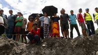 More than a dozen people on the edge of a muddy and rocky cliff seen from below, some looking downward.