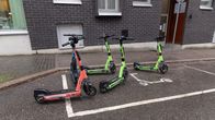 Five rentable e-scooters standing at a designated scooter parking zone, one of the devices is halfway out of the parking spot.