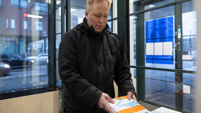 Mies pudottaa paperipakettia Kelan konttorilla palautuslaatikkoon.