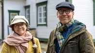  Paret står utomhus framför det vita skolhuset med gröna fönsterkarmar.