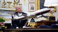 Trump istuu työhuoneessaan ja etualalla on virkakoneen pienoismalli.
