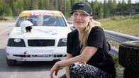 Stuntnäyttelijä Ansko Pitkänen katsoo kameraan. Takana näkyy ralliauto, jonka konepellillä on kypärä. 
