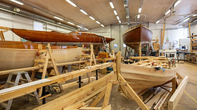 En båtverkstad med flera träbåtar under byggnation och reparation.
