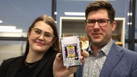 Mies seisovat ja pitävät kädessään suorakulmion muotoista mikroskooppia, jonka keskellä on pyöreä linssi.