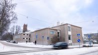 En byggnad av betongelement invid en korsning. Fasaden har fönster i olika storlekar och bilar kör framför byggnaden.