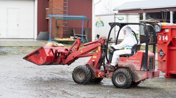 person i skyddsdräkt kör minilastare