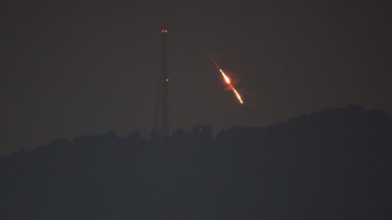 A nighttime image showing a dark sky, a mast with red lights and a rocket descending toward earth. 