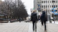 En dimmig vinterdag på en gågata med två personer i rörelse, omgivna av träd och byggnader.