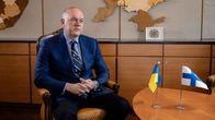Ukraine’s ambassador to Finland, Mykhailo Vydoinyk, sitting in a chair at the Ukrainian embassy. On the table there is a Ukrainian and Finnish flag.
