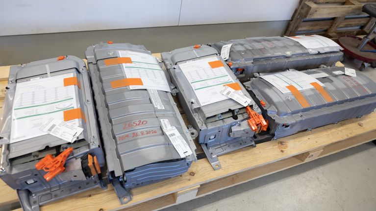 Fyra stora litiumjonbatterier med fastsatta dokument och orangefärgade etiketter ligger på en träpall inomhus.