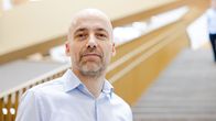 Lauri Parkkonen katsoo kameraan. Taustalla on Aalto yliopiston aulaa ja portaikkoa.