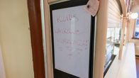 Seinällä on paperilappu, jossa lukee "Kiitos kaikille asiakkaille!". Taustalla näkyy kahvilan vitriinejä.