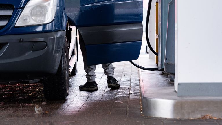 Sininen pakettiauto tankkauspisteellä, auton vieressä seisoo henkilö, jonka jalat näkyvät oven takaa.