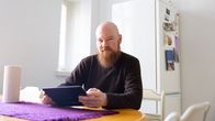 Lars Hobin pitelee tablet-tietokonetta keittiön pöydän ääressä ja takana on jääkaappi. 