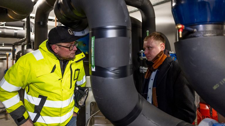 Qheatin Rami Niemi ja Avaran Alexandre Zaitsev katsovat toisiinsa lämmönjakohuoneessa. Kuvassa miesten välissä etualalla kulkee iso musta putki. 