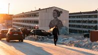 Lumisessa auringonlaskussa mies ylittää kadun, taustalla kerrostalon seinään maalattu muraali.
