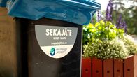 Tumma sekajäteastia kuvattuna kesäisenä päivänä. Roska-astian kyljessä on teksti "sekajäte".