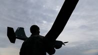 Kuvassa henkilö esittää dronea harmaata taivasta vasten.