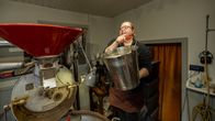 En kvinna arbetar med att rosta kaffe i en kafferosteri. Kaffe hälls från en hink i rostningsmaskinen för att tillagas.