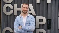 En person med ljust hår och jeansskjorta står framför en vägg med stora bokstäver och siffran 11.