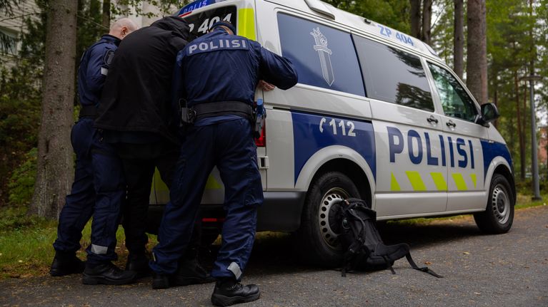 Poliisiopiskelijoiden rikospaikkaharjoitus. Kaksi poliisia pitävät kiinni otettua henkilöä poliisiautoa vasten.