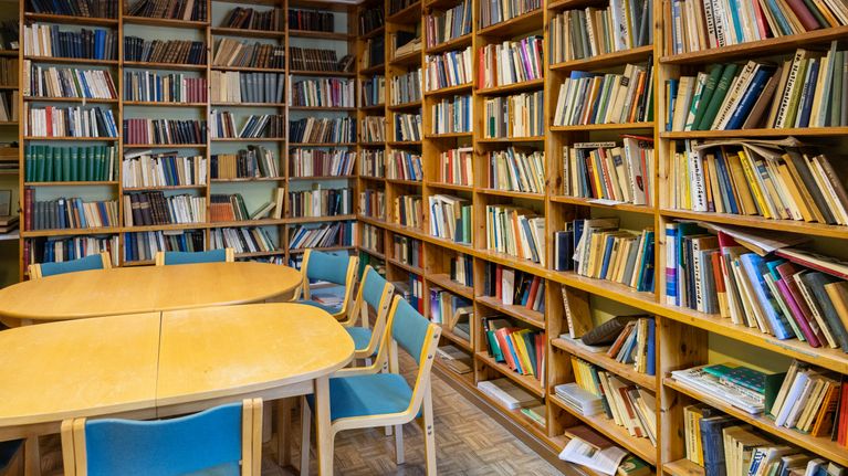 Ett bibliotek med flera bokhyllor fyllda med böcker och ett bord med stolar framför.