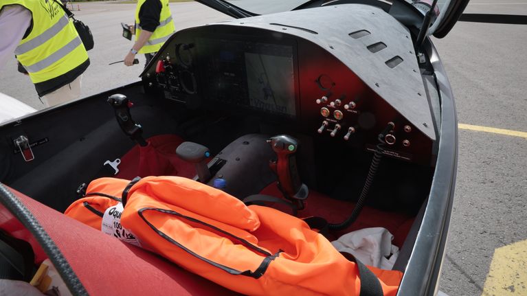 View into the cockpit of a small airplane with two people wearing yellow vests to the left. 