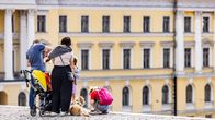 Two parents, two children and a dog seen from behind at the top of a staircase at Helsinki's Senate Square on a sunny  day.