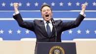 Elon Musk seisoo puhujankorokkeella ja elehtii kädet ylös nostettuina ja huutaa yleisölle.