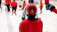 En hockeyjunior i hjälm tittar ut över rinken. I bakgrunden fler unga spelare.