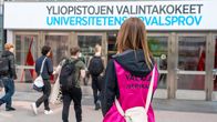 Yliopistojen valintakokeisiin osallistujia saapumassa koepaikalle, koetta valvomassa henkilökuntaa.