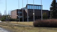 En brun tegelbyggnad. Framför byggnaden står en rad med flaggstänger.