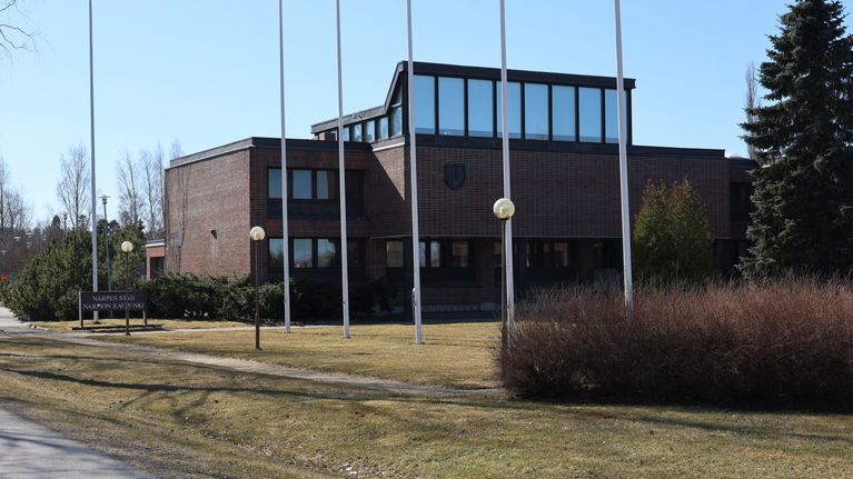 En brun tegelbyggnad. Framför byggnaden står en rad med flaggstänger.