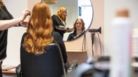 Kampaamon peilinkautta näkyy, että kampaaja kampaa asiakkaan hiuksia. 