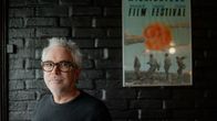 Elokuvaohjaaja Alfonso Cuaron seisoo mustan tiiliseinän edessä ja hymyilee kameralle, takana Sodankylän elokuvajuhlien juliste.