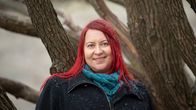 Kirjailija Hanna Lantto seisoo lumisateessa,  vanhan pajun oksien edessä, yllään tumma takki ja sininen huivi. Hänen hiuksensa ovat punaiset.