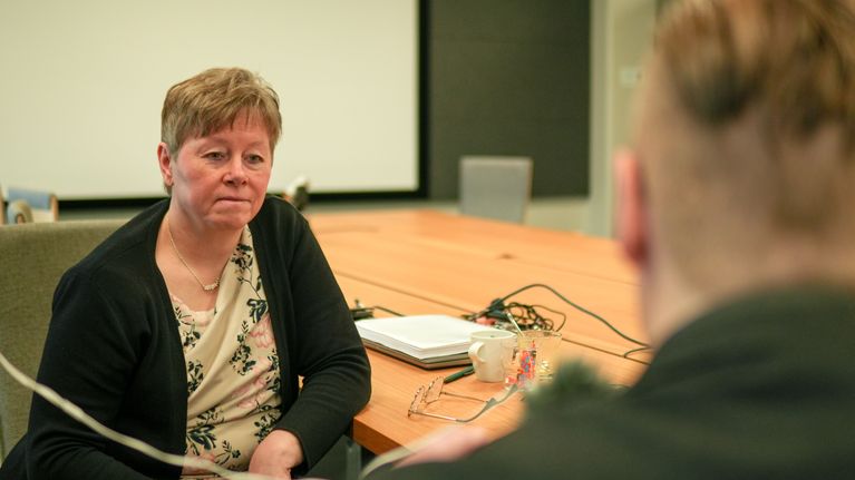 Två personer sitter vid ett konferensbord med dokument och en kaffekopp framför sig.