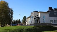 Valkoinen tiilirakennus jonka seinässä Pelkosenniemen kunnan vaakuna ja teksti kunnantalo, pihalla muutama auto.