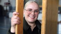 Oona Tammisto pitää puista liikuntasalin penkkiä pystyssä ja katsoo kameraan.