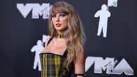 Taylor Swift poserar i en rutig klänning framför en svart vägg. Hon tittar åt sidan.