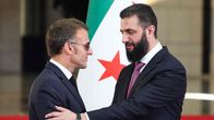Emmanuel Macron ja Ahmad al-Šaraa kättelevät Syyrian lipun edessä.