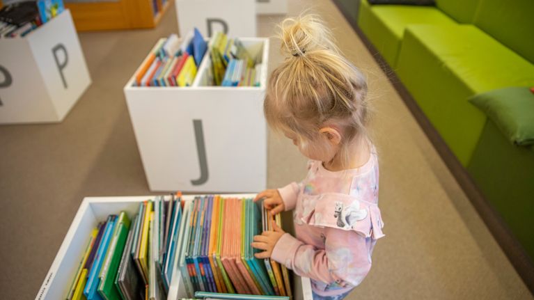 Lapsi tutkii kirjastossa  kirjoja.