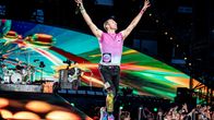 Chris Martin laulaa mikkiin lavalla. Taustalla näkyy Parken stadionin rakenteita ja yleisön muodostama valomeri.