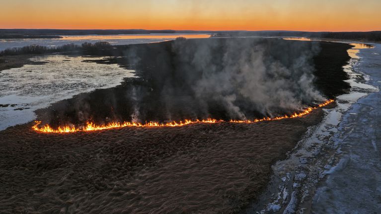 Ilmakuva, jossa näkyy Tornionjoen Likasaari myöhäisenä kevätiltana ja koko saaren poikki yltävä liekkirintama, josta nousee savua.