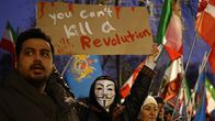 En demonstrant som bär en mask håller upp en skylt där det står "you can´t kill a revolution".