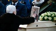 Henkilö koskettaa arkun päälle aseteltua valokuvaa.