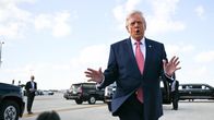 Donald Trump puhuu medialle lentokentällä, taustalla näkyy autoja ja turvamiehiä kiitoradalla.