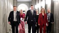 Kuusi henkilöä kävelee rivissä eduskunnan käytävällä.