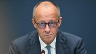 Friedrich Merz pukeutuneena tummansiniseen pukuun, valkoiseen paitaan ja silmälaseihin istuu mikrofonin edessä tummansinistä taustaa vasten.