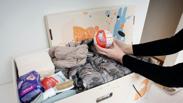 A woman is holding a small soft ball, over a baby box/ maternity package.